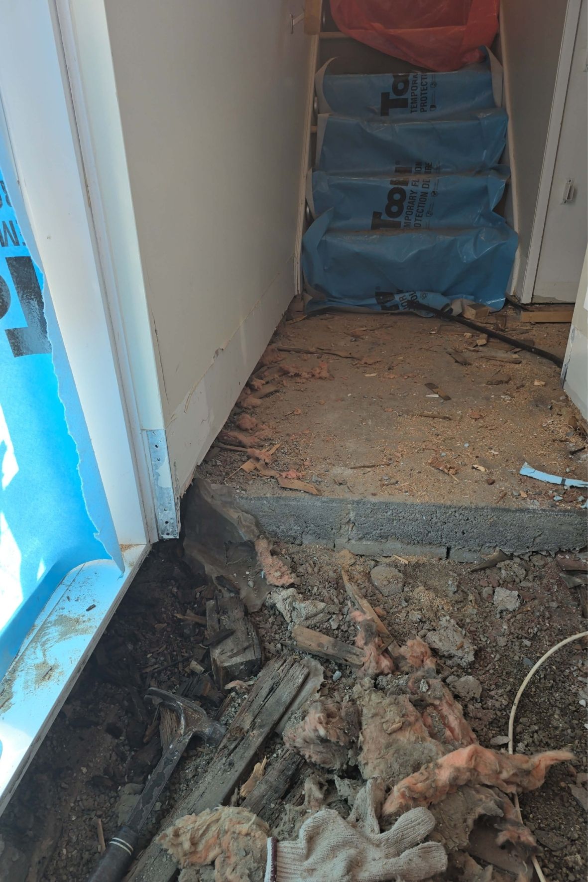 Escalier protégé par bâches plastiques et débris au sol dans un chantier intérieur  dans le West Island